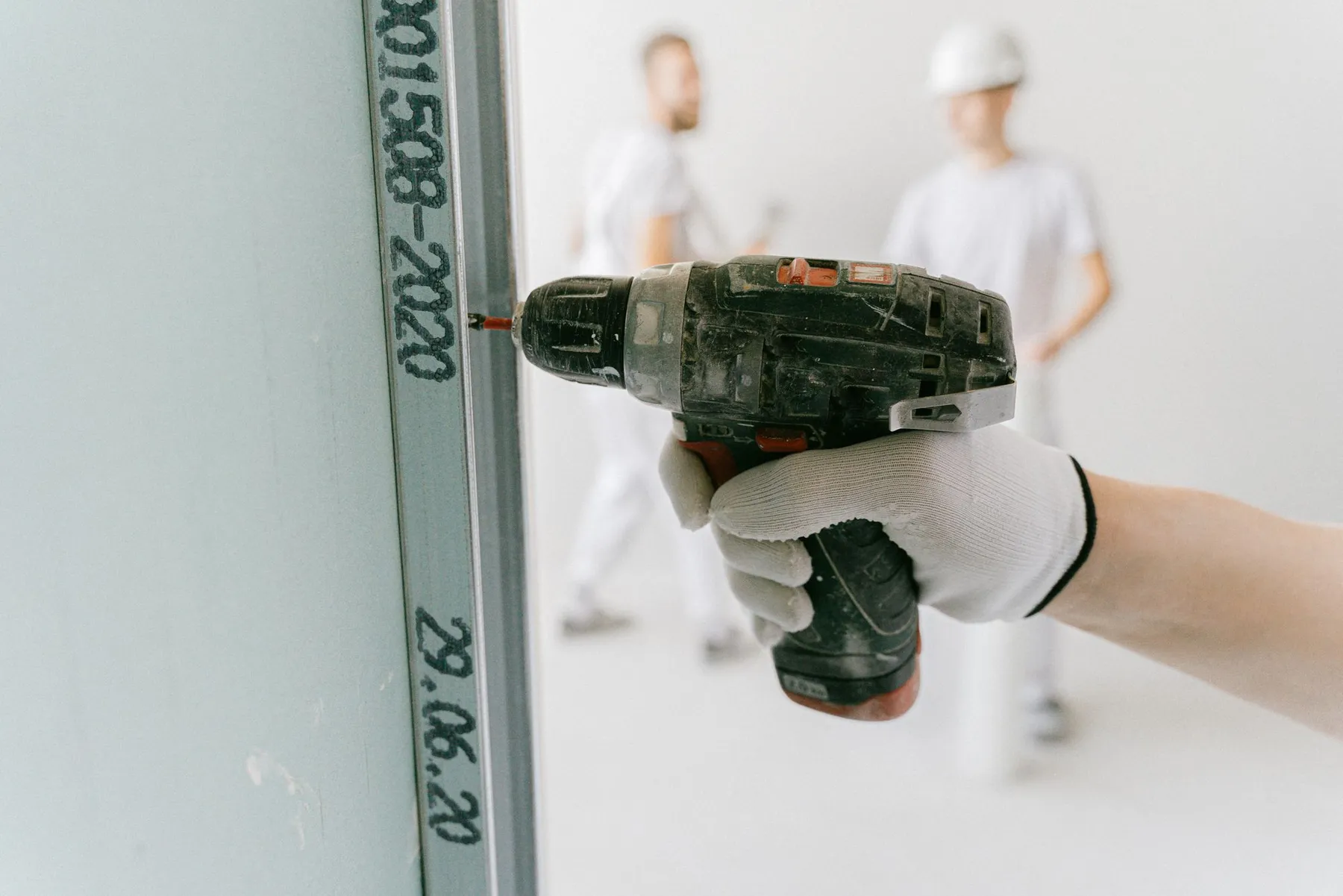Construction worker in a hard hat and gloves drilling into plasterboard on a commercial interior fit-out