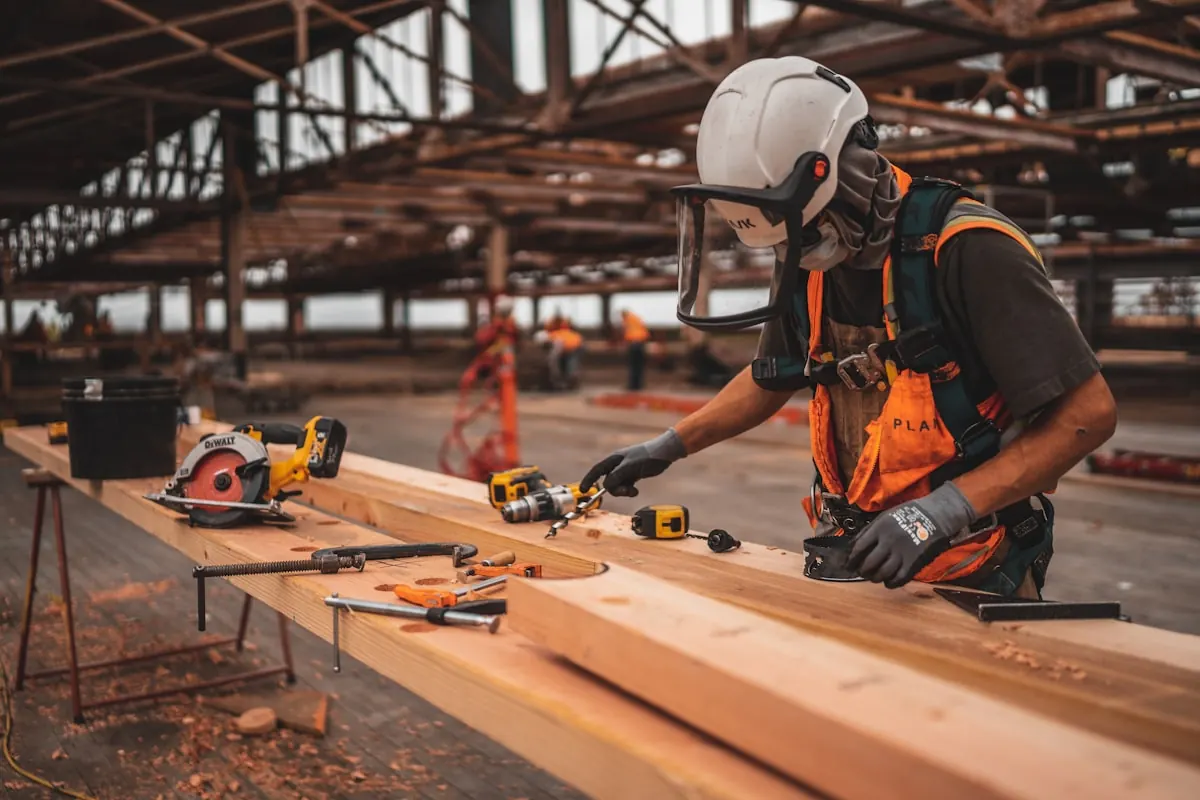 Carpenter in a hard hat, visor and hi-vis measuring timber on a site workbench